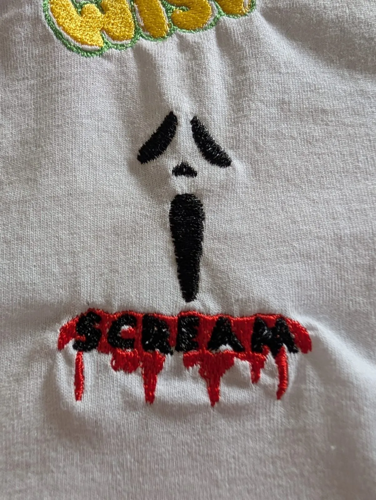 Close-up of a black-and-red embroidered face and dripping lettering on white fabric