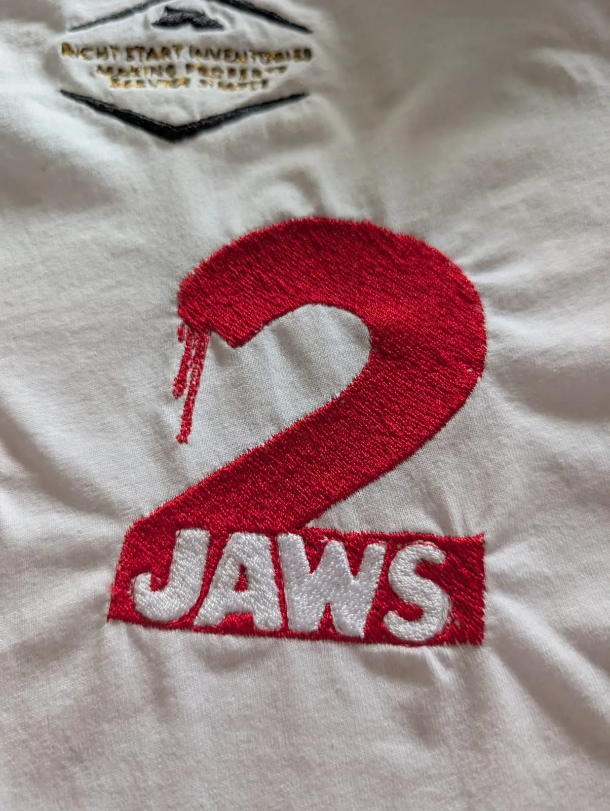 Close-up of a red embroidered shark graphic with white ‘JAWS’ lettering