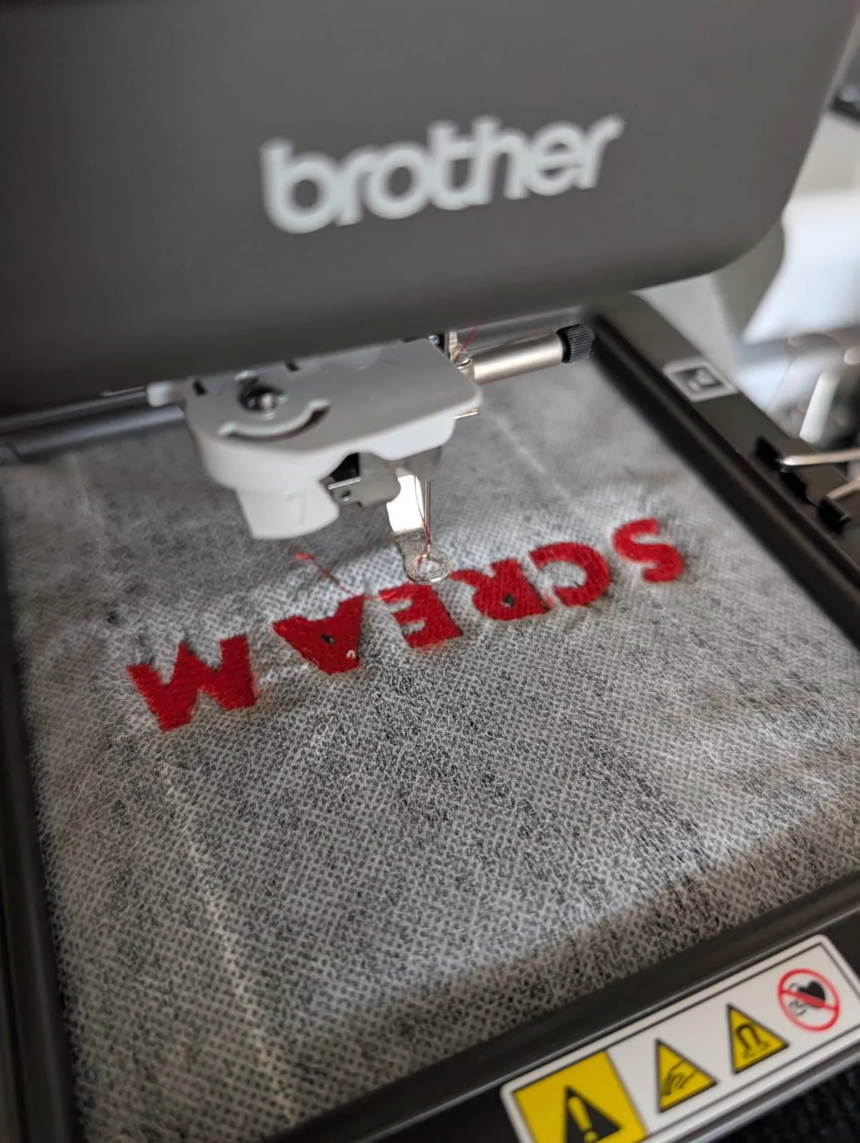 Close-up of a sewing machine stitching red lettering into grey fabric