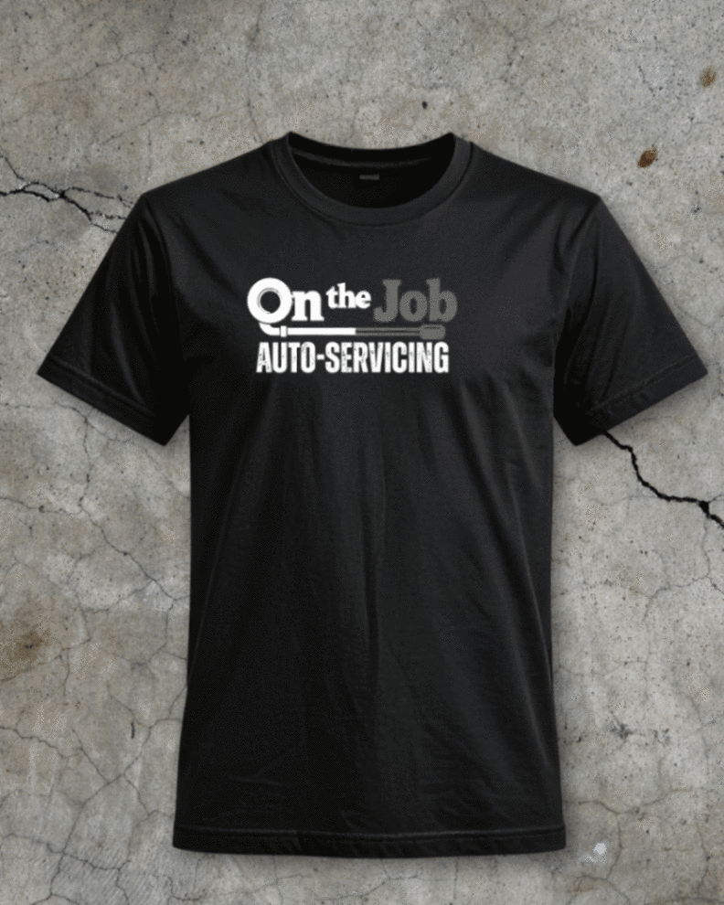 Black T-shirt printed with On the Job Auto-Servicing lettering, photographed on cracked concrete