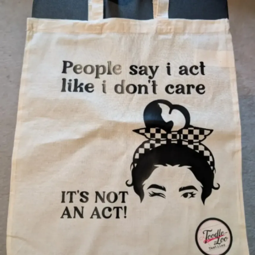 Cream tote bag with a black illustrated face and the custom message People say I act like I don't care