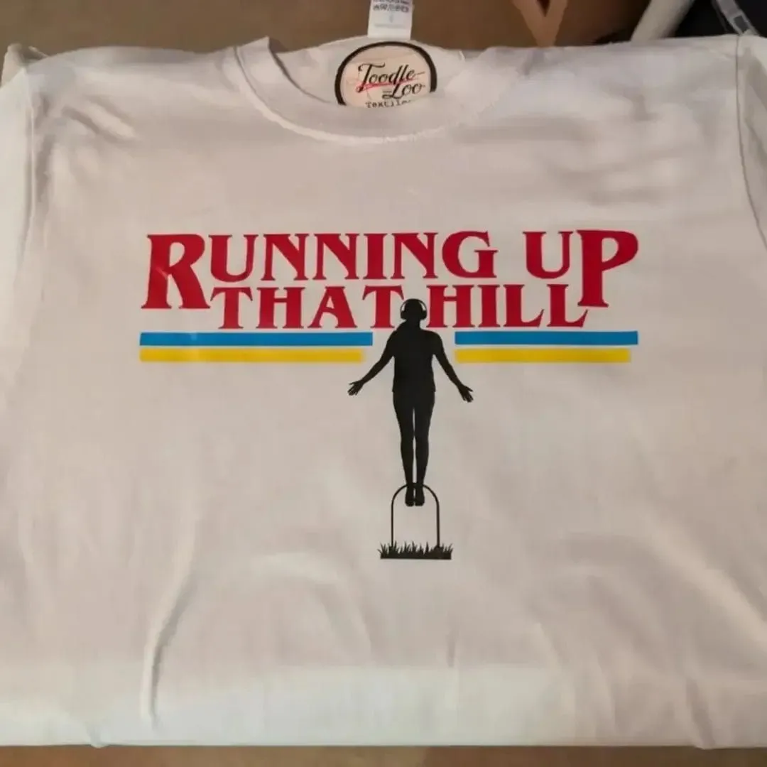 White T-shirt with Running Up That Hill lettering and a silhouetted figure